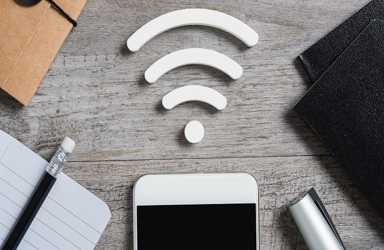 Top view of smartphone on desk searches a free wifi connection available. High angle view of smart phone with white wi-fi sign on top. Internet technology and networking concept.